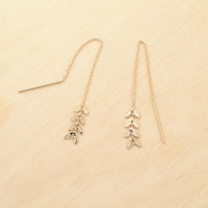 May include: A pair of gold-colored threader earrings. Each earring features a delicate chain with a cluster of three leaf-shaped charms. The earrings have a simple, elegant design, perfect for everyday wear.