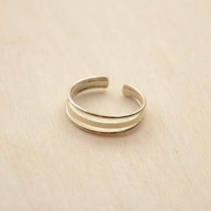 Op de afbeelding: Een gouden teenring met een dubbelband ontwerp. De ring heeft een getextureerd oppervlak.