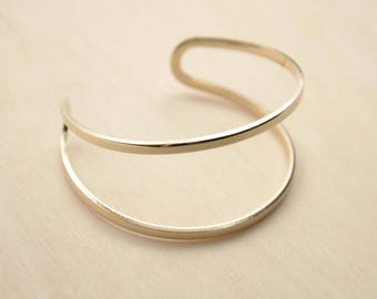 May include: A gold-toned double-band bangle bracelet. The bracelet is made of two thin bands of metal that are joined together at the ends.