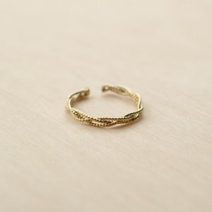 May include: A gold-toned ring with a braided design. The ring is made of multiple strands of metal that are twisted together.