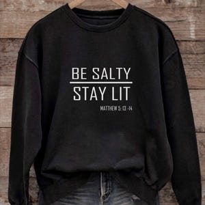 May include: Black sweatshirt with white text that reads "BE SALTY STAY LIT" and "MATTHEW 5:13-14".
