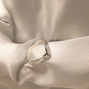 May include: A silver ring with a textured, slightly rounded band.