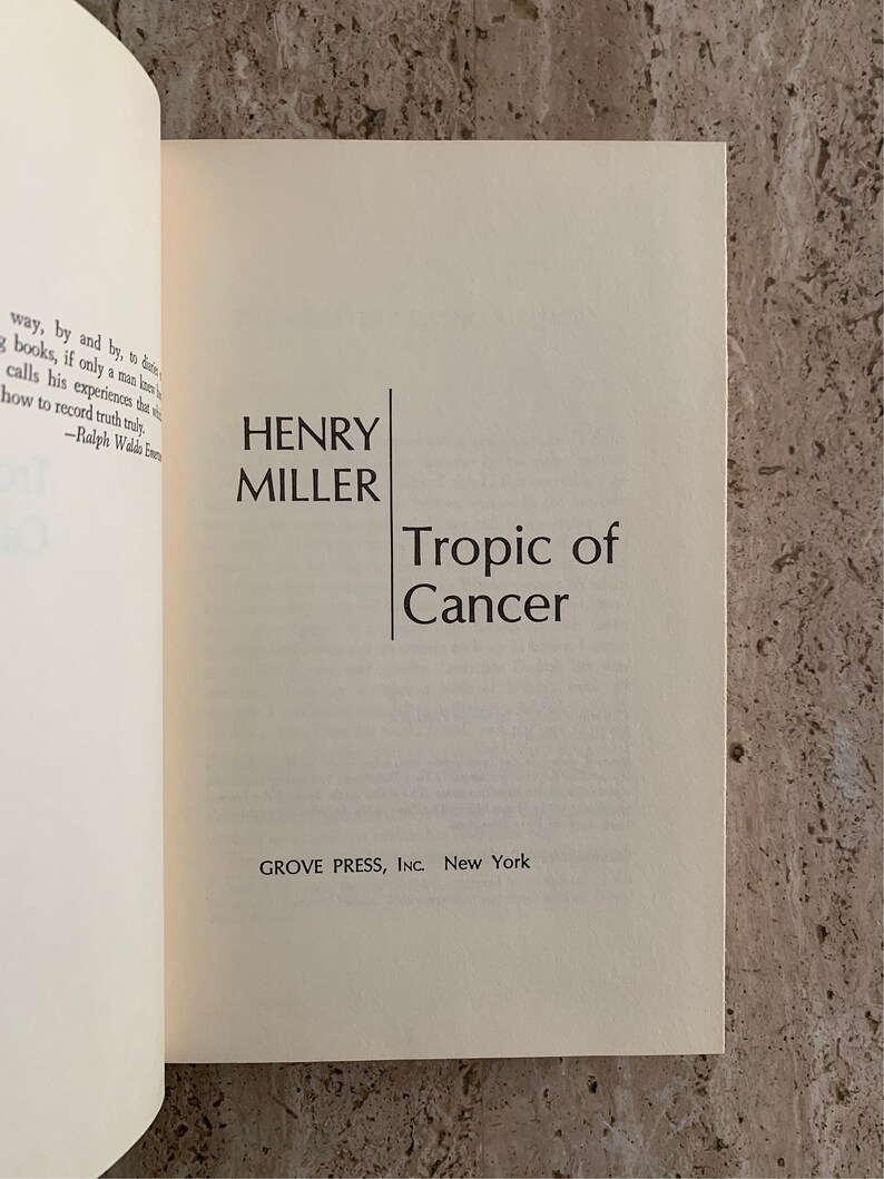 May include: A white book with black text on the cover. The title is "Tropic of Cancer" by Henry Miller. The book is published by Grove Press, Inc. in New York.