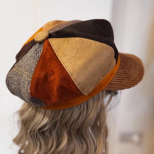 May include: A multi-textured newsboy cap featuring a patchwork design of brown corduroy, tan suede, dark brown fabric, and a grey herringbone wool pattern. The cap includes a central fabric-covered button and a brown corduroy brim.
