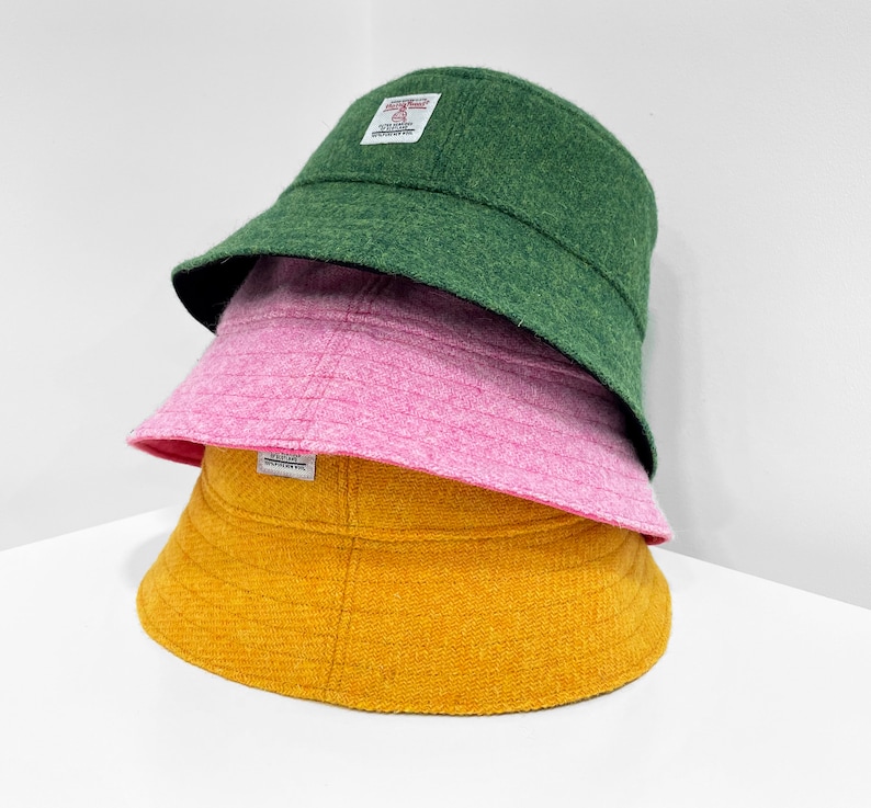 May include: Three bucket hats stacked on top of each other. The top hat is green, the middle hat is pink, and the bottom hat is yellow.