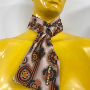 Pu&ograve; includere: Un foulard di seta con motivo marrone, arancione e blu con un'etichetta in metallo dorato che dice "STERN & CO. NY"