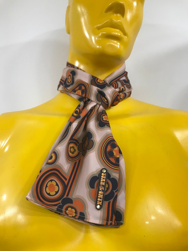 Pu&ograve; includere: Un foulard di seta con motivo marrone, arancione e blu con un'etichetta in metallo dorato che dice "STERN & CO. NY"