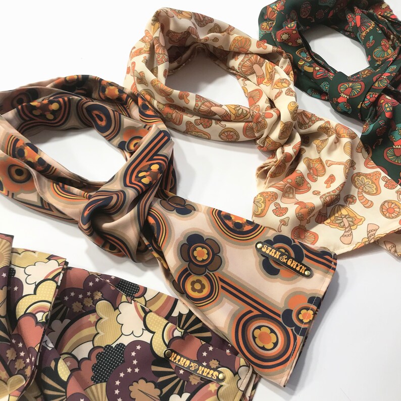 Pu&ograve; includere: Tre foulard di seta con motivi diversi. I foulard sono beige con disegni marroni, arancioni e gialli. Un foulard ha un motivo a fungo, un altro ha un motivo floreale e il terzo ha un motivo geometrico. Ogni foulard ha un'etichetta dorata con il testo "Sean & Rhys".