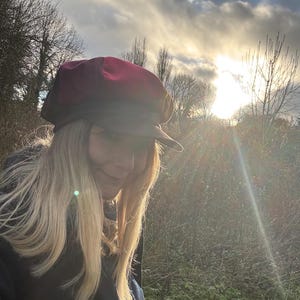 May include: A multi-colored newsboy cap featuring a deep red crown and a dark brown brim. The hat has a structured, rounded top with a short, stiff visor extending from the front, crafted with visible paneling and a solid, opaque fabric finish.