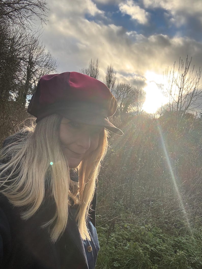 May include: A multi-colored newsboy cap featuring a deep red crown and a dark brown brim. The hat has a structured, rounded top with a short, stiff visor extending from the front, crafted with visible paneling and a solid, opaque fabric finish.