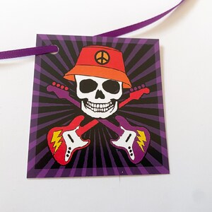 May include: A purple and black tag with a skull wearing an orange hat with a peace sign. The skull is holding two guitars that are crossed. The tag has a hole in the top for a ribbon.