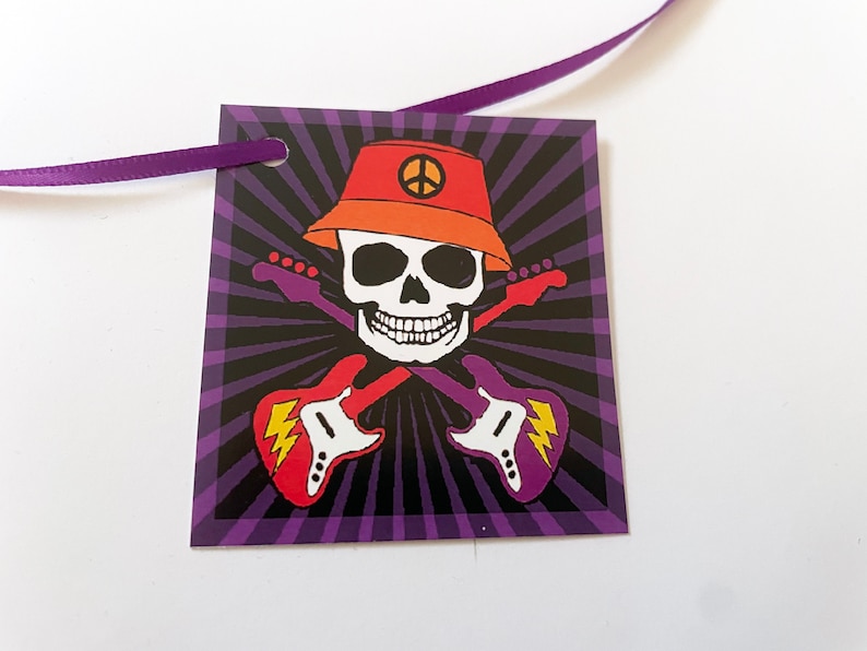 May include: A purple and black tag with a skull wearing an orange hat with a peace sign. The skull is holding two guitars that are crossed. The tag has a hole in the top for a ribbon.