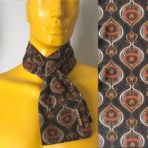 Op de afbeelding: Een bruine en gouden zijden sjaal met een paisley-patroon. De sjaal heeft een label met de tekst "Silk & Onyx".