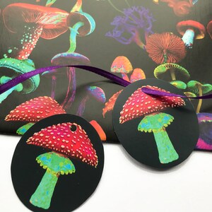 Puede incluir: Papel de regalo y etiquetas de regalo negros con un dise&ntilde;o de setas colorido. El papel de regalo presenta una variedad de setas en rojo, verde, morado y naranja. Las etiquetas de regalo son redondas con un dise&ntilde;o de seta roja y blanca y una cinta morada.