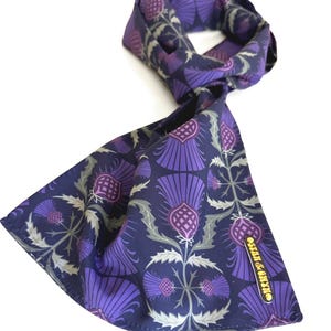 May include: A navy blue silk scarf with a purple thistle pattern. The scarf has a gold label that says "Silk & Cotton".