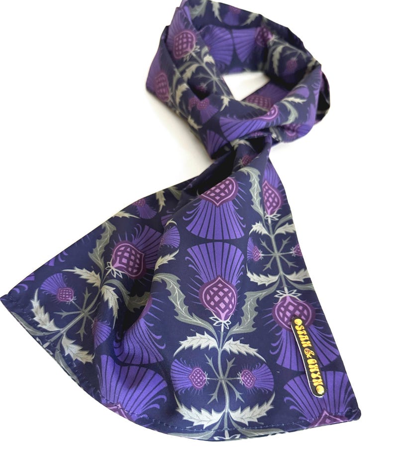 May include: A navy blue silk scarf with a purple thistle pattern. The scarf has a gold label that says "Silk & Cotton".