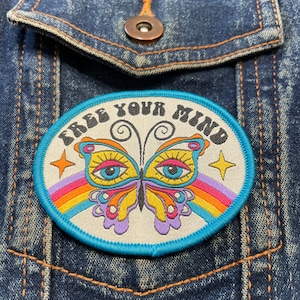 May include: A blue and white embroidered patch featuring a rainbow and butterfly design. The text "Free Your Mind" is written in a retro font.