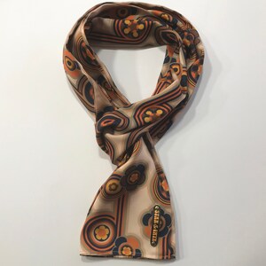 Pu&ograve; includere: Un foulard di seta beige con un motivo floreale e geometrico retr&ograve; in tonalit&agrave; arancio, marrone e blu. Il foulard ha una piccola etichetta dorata con il testo "Stark & River".