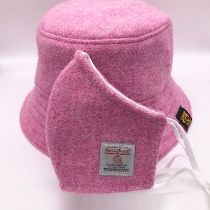 May include: Pink bucket hat made of Harris Tweed with a matching pink face mask. The hat has a white label with the text "HAND WOVEN CLOTH Harris Tweed&reg; OUTER HEBRIDES OF SCOTLAND 100% PURE NEW WOOL".