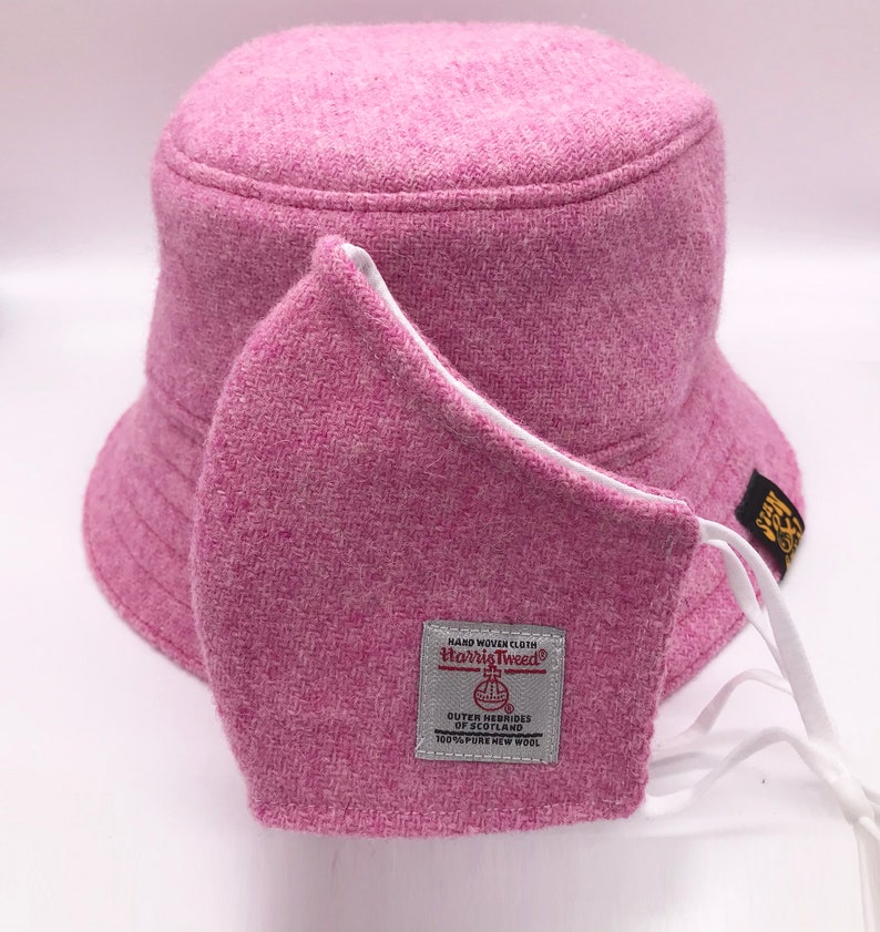 May include: Pink bucket hat made of Harris Tweed with a matching pink face mask. The hat has a white label with the text "HAND WOVEN CLOTH Harris Tweed&reg; OUTER HEBRIDES OF SCOTLAND 100% PURE NEW WOOL".