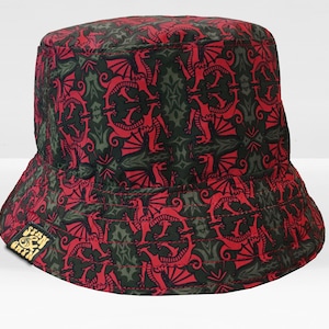 May include: A red and green bucket hat with a dragon pattern. The hat has a black brim and a small label with the text "Stay & Chin" in yellow.
