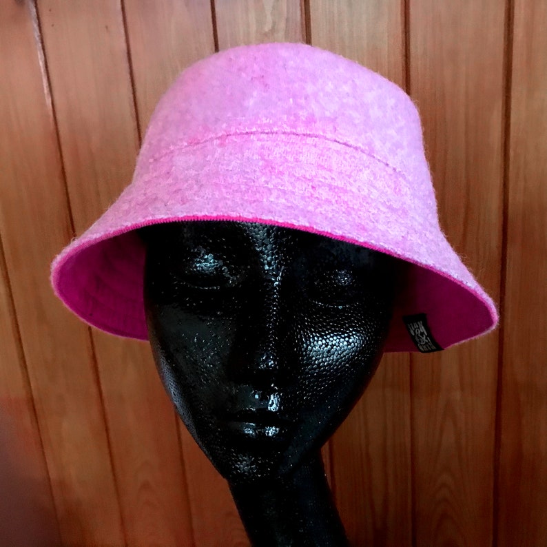 May include: A pink bucket hat with a fuzzy texture and a pink lining. The hat is on a black mannequin head.