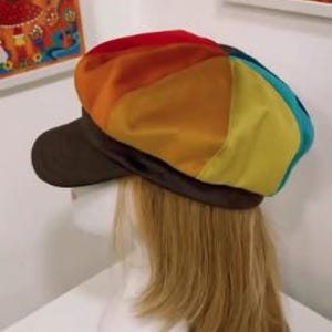 May include: A newsboy cap featuring a multi-colored panel design with segments of red, orange, yellow, and teal. The cap includes a solid dark brown brim and a matching dark brown band encircling the base, providing a distinct contrast to the vibrant, segmented crown.