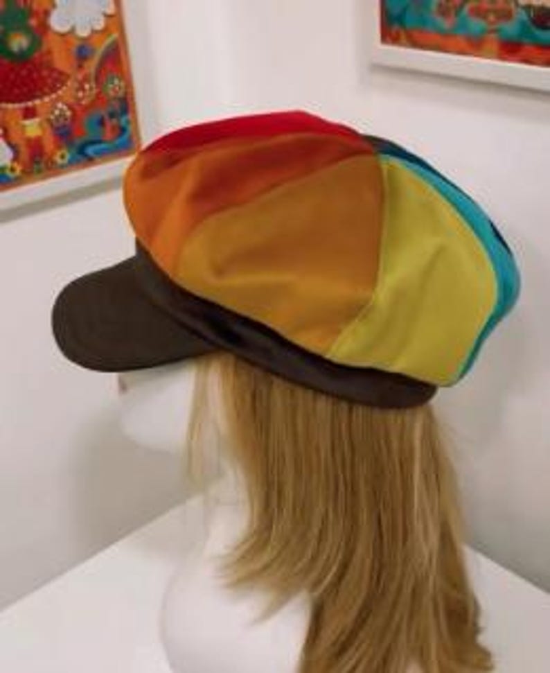 May include: A newsboy cap featuring a multi-colored panel design with segments of red, orange, yellow, and teal. The cap includes a solid dark brown brim and a matching dark brown band encircling the base, providing a distinct contrast to the vibrant, segmented crown.