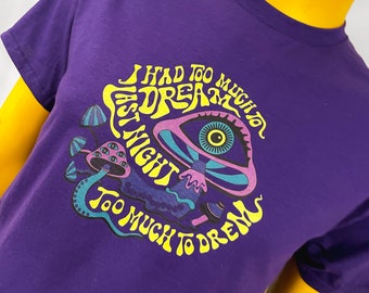 May include: Purple t-shirt with a psychedelic mushroom design and the text "I had too much to dream last night too much to dream".