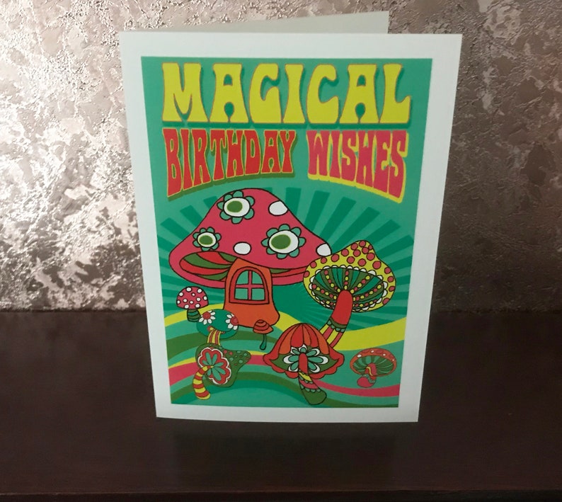 Op de afbeelding: Een groene kaart met de tekst "Magical Birthday Wishes" in gele en rode letters. De kaart heeft een cartoonillustratie van kleurrijke paddenstoelen met witte stippen.