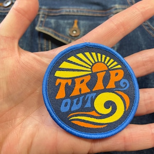 May include: A blue, orange, and yellow embroidered patch with a sun, waves, and the text "TRIP OUT".