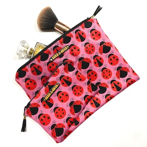 May include: Two pink zippered makeup bags with a ladybug print. The larger bag has the text "Sarah & Olivia" in gold lettering. The smaller bag has the same text in gold lettering.