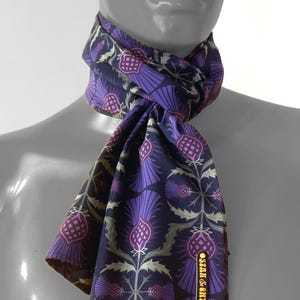 May include: A purple and green patterned silk scarf with a gold label that reads "STAN & KYNN".