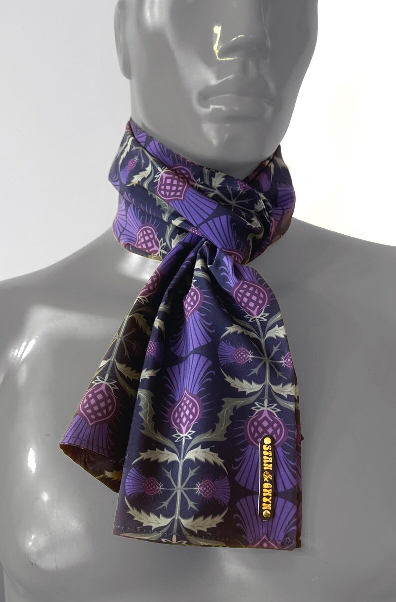 May include: A purple and green patterned silk scarf with a gold label that reads "STAN & KYNN".