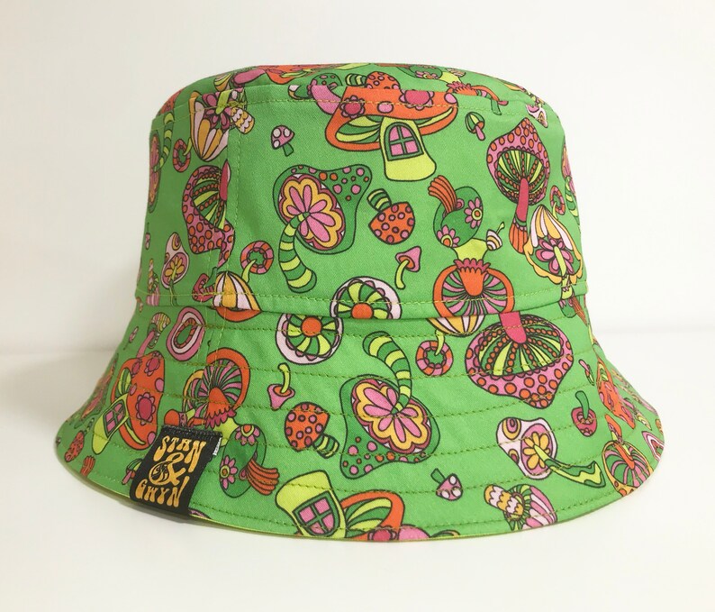 May include: Green bucket hat with a psychedelic mushroom print. The hat has a black label with the text "Stan & Bryn".