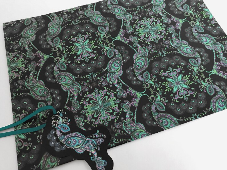 K&ouml;nnte beinhalten: Schwarzes Geschenkpapier mit einem Pfauenmuster in Gr&uuml;n- und Lilat&ouml;nen. Das Papier hat ein Paisley-Muster mit filigranen Details.