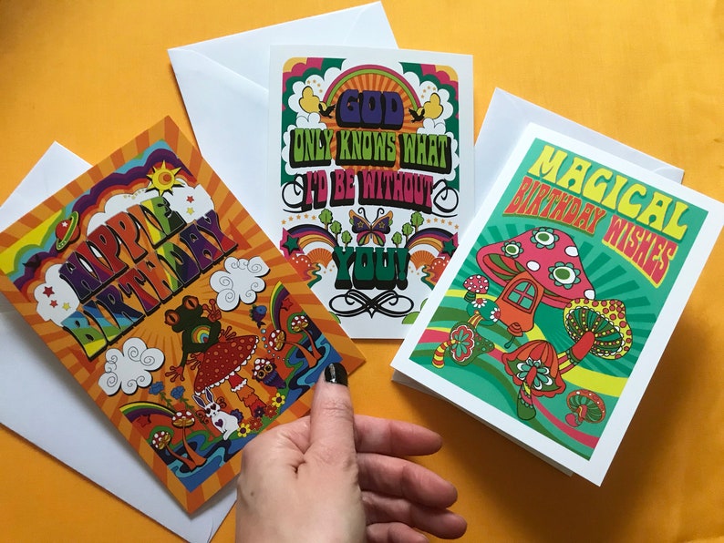 Op de afbeelding: Drie kleurrijke wenskaarten met psychedelische ontwerpen. De eerste kaart heeft een regenboogachtergrond met de tekst "Happy Birthday" in een groovy lettertype. De tweede kaart heeft een groene achtergrond met de tekst "God Only Knows What I'd Be Without You!" in een psychedelisch lettertype. De derde kaart heeft een groene achtergrond met de tekst "Magical Birthday Wishes" in een psychedelisch lettertype.