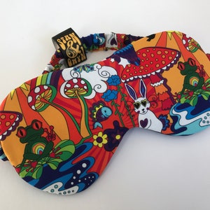 Könnte beinhalten: Eine farbenfrohe Schlafmaske mit einem psychedelischen Design mit Pilzen, Fröschen, einem Kaninchen und Blumen. Die Maske hat ein Gummiband und ein Etikett mit der Aufschrift "Stan & Bryn".