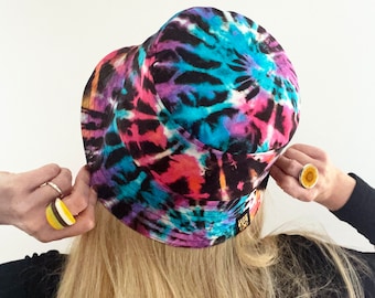 May include: A black bucket hat with a tie-dye pattern in shades of pink, blue, and purple. The hat has a small gold label with the text "Sash & Co."