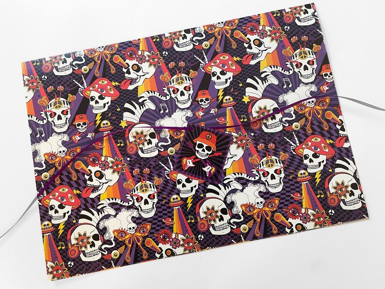 May include: A colorful wrapping paper with a psychedelic skull pattern. The skulls are wearing headphones, sunglasses, and have multiple eyes. The background is a mix of black, purple, orange, and yellow.