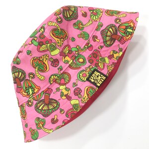 May include: Pink bucket hat with a mushroom and flower pattern. The hat has a red underside and a small green and yellow patch with the text "Green & Grey" on it.