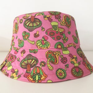 May include: Pink bucket hat with a mushroom print. The mushrooms are in various shades of green, yellow, orange, and red.