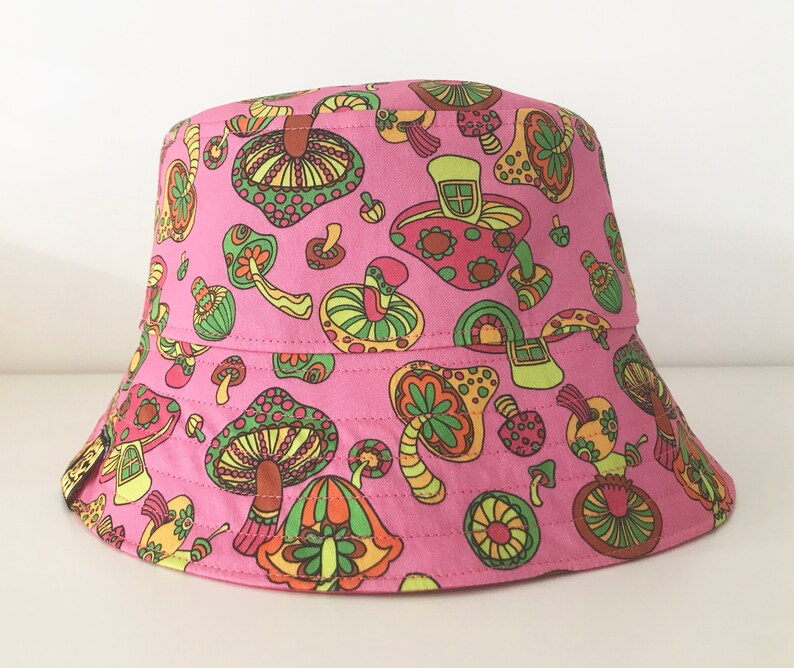May include: Pink bucket hat with a mushroom print. The mushrooms are in various shades of green, yellow, orange, and red.