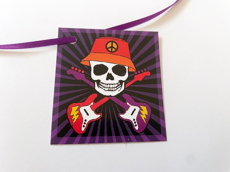 May include: A purple and black tag with a skull wearing an orange hat with a peace sign. The skull is holding two guitars that are crossed. The tag has a hole in the top for a ribbon.