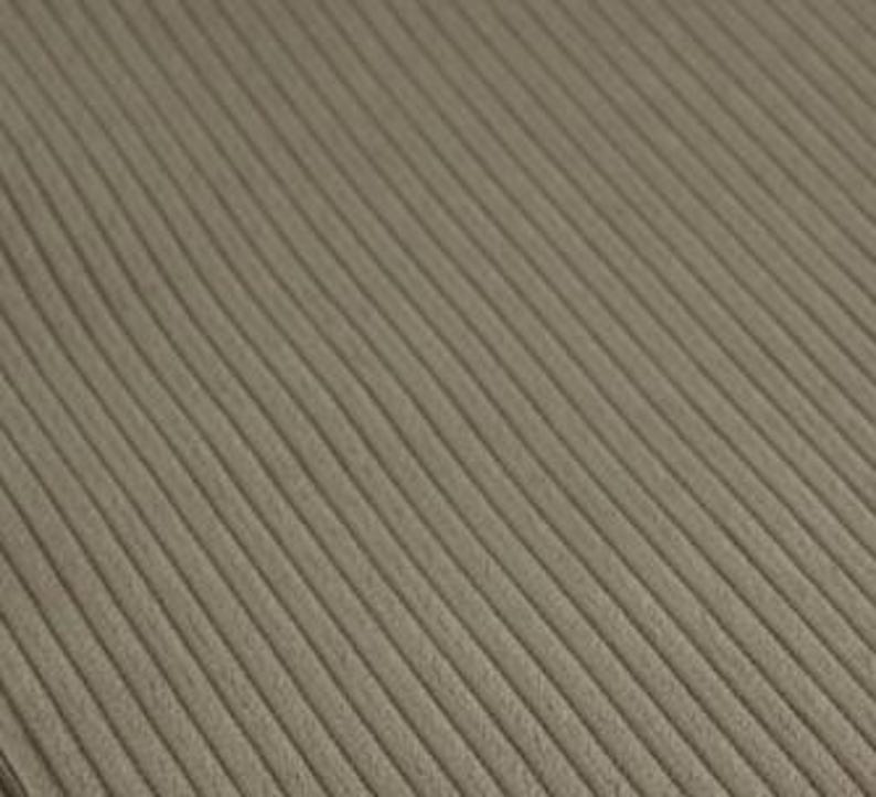 May include: A taupe-colored fabric featuring a distinct corduroy texture with parallel, raised vertical ridges running diagonally across the surface. The material displays a consistent, muted earthy tone with a soft, matte finish throughout.