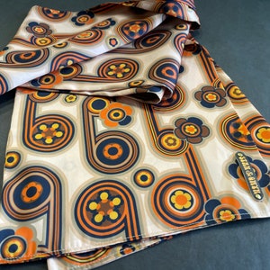 Pu&ograve; includere: Un foulard di seta beige con un motivo retr&ograve; di cerchi e fiori arancioni, marroni e blu. Il foulard ha un piccolo cartellino dorato con il testo "seam & onyx".