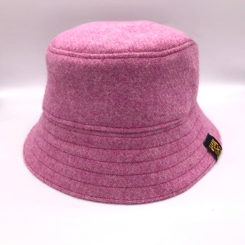 May include: A pink bucket hat with a black and gold logo on the side.