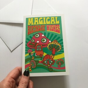Op de afbeelding: Een kaart met een psychedelisch ontwerp met paddenstoelen en de tekst "Magical Birthday Wishes".