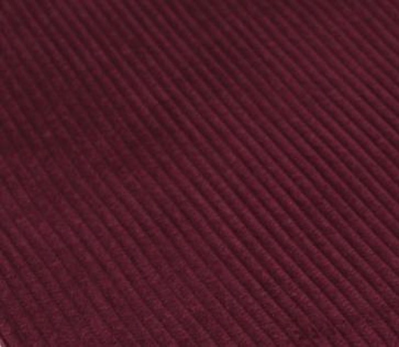 May include: A deep burgundy fabric featuring a distinct corduroy texture with parallel vertical ridges running diagonally across the frame. The material displays a consistent dark red hue with subtle shadows between the raised lines of the fabric.