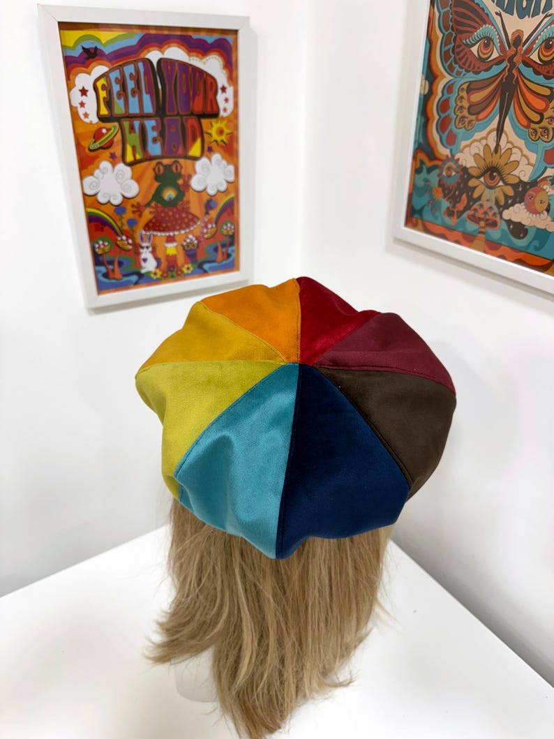 May include: A multi-colored beret constructed from eight triangular panels of velvet fabric. The hat features a vibrant spectrum of colors including orange, yellow, lime green, light blue, dark blue, brown, maroon, and red, arranged in a circular pattern.